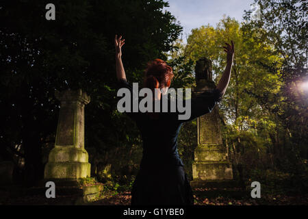 Eine rothaarige Frau oder Hexe ist, hob die Arme und Durchführung ein Rituals ein Grab Stockfoto