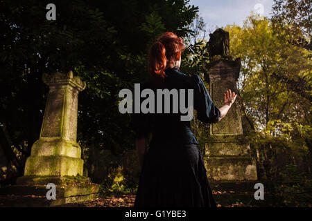 Eine rothaarige Frau oder Hexe ist, hob die Arme und Durchführung ein Rituals ein Grab Stockfoto