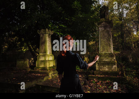 Eine rothaarige Frau oder Hexe ist, hob die Arme und Durchführung ein Rituals ein Grab Stockfoto