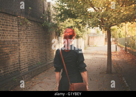 Eine junge rothaarige Frau in einer gepflasterten Gasse im Herbst an einem sonnigen Tag Fuß Stockfoto