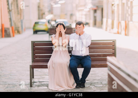 Junge Frau und Mann sitzt auf der Bank, die Augen mit den Handflächen schließen Stockfoto