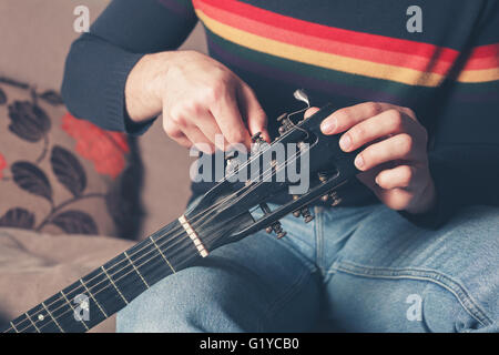 Ein junger Mann sitzt auf dem Sofa und ist eine Gitarre tuning Stockfoto