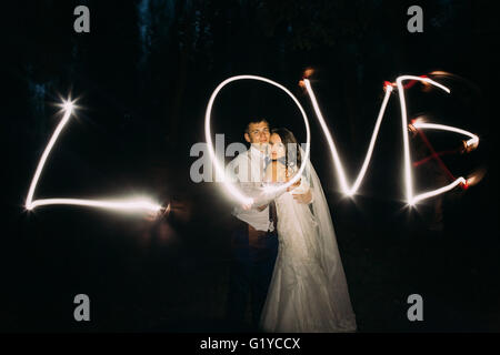 Umarmend verheiratet paar und Licht Malerei des Wortes Liebe auf Hintergrund Stockfoto