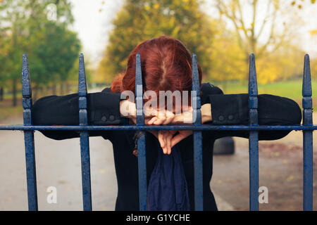 Eine traurige Frau ruht ihr Kopf auf ein Tor in den Park im Herbst Stockfoto