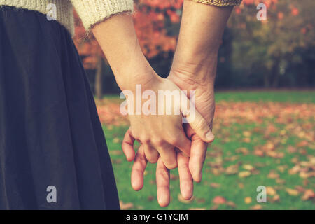 Schließen Sie bis auf ein paar Hand in Hand im Park im Herbst Stockfoto