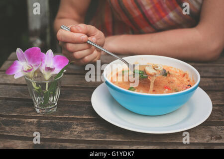 Eine junge Frau ist auf einen Tisch draußen Tom Yum Suppe essen.