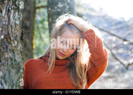 Junges Mädchen mit langen blonden Haaren, die an einen Baum gelehnt