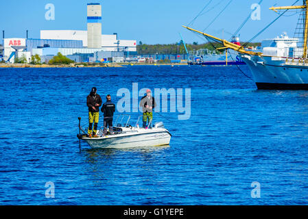 Karlskrona, Schweden - 5. Mai 2016: Drei junge Erwachsene Männer Stand in einen Halbmond Motorboot Angeln mit Rute und anzugehen. Alten Segeln s Stockfoto