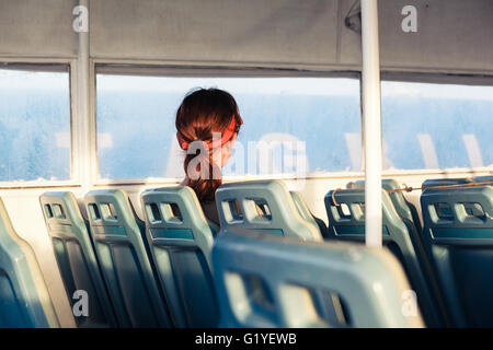 Eine junge Frau sitzt alleine auf einer Fähre Stockfoto