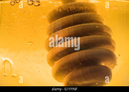 Hölzerne Honig Dipper in Glas Jar of Honey mit Luftblasen Stockfoto
