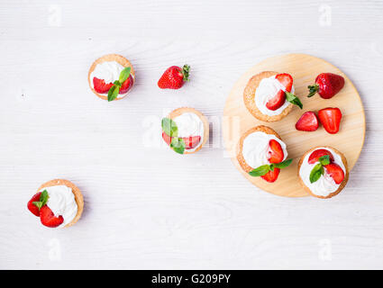 Hausgemachte Buttercreme Cupcakes mit Erdbeeren und frischer Minze auf weißer Holztisch von oben gesehen Stockfoto