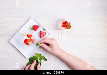 Platzieren von Minzblatt auf der Oberseite eine Schicht Biskuit mit Erdbeeren in ein Glas, von oben gesehen Stockfoto