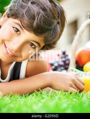 Closeup Portrait von niedlich fröhlicher Junge auf frischen grünen Wiese liegend, mit Obst zum Frühstück, Sommerferien genießen Stockfoto