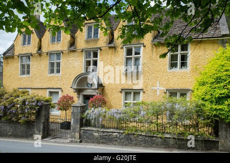 Blühende Glyzinie auf dem Zaun ein gelbes Haus in Castle Combe, Chippenham, Wiltshire, England Stockfoto