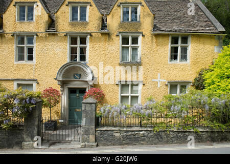 Blühende Glyzinie auf dem Zaun ein gelbes Haus in Castle Combe, Chippenham, Wiltshire, England Stockfoto