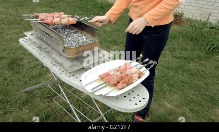 Mädchen setzt Feuerschale Grill-Spieße mit Fleisch Stockfoto