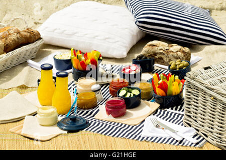Sommer-Picknick am Strand. Portion Picknick Utensilien mit Gemüse und Saucen auf gestreiften Tischdecken und gestrickte Kissen blau. S Stockfoto