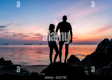 Silhouette junges Paar stehen am Strand Händchenhalten und den tropischen Sonnenuntergang Stockfoto