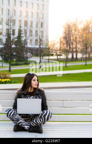 Schüler sitzen auf Bank, Musik hören und mit Laptop gegen Universität Campus wegschauen Stockfoto