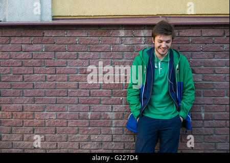 Gemeinsamen junger Mann trägt grün-t-Shirt-Jacke und Jeans gegen eine rote Mauer auf die Kamera Stockfoto