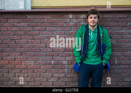 Gemeinsamen junger Mann trägt grün-t-Shirt-Jacke und Jeans gegen eine rote Mauer auf die Kamera Stockfoto