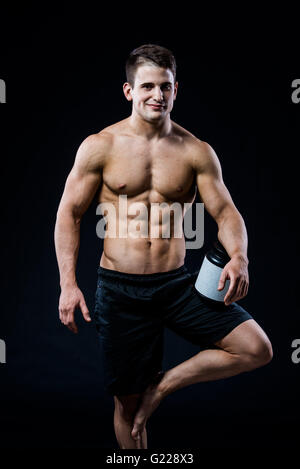 Bodybuilding und Sport Thema: schön stark Bodybuilder halten Kunststoff-Glas mit einem trockenen Protein Gefühl entspannt isolierten auf schwarzen Hintergrund im Studio Stockfoto