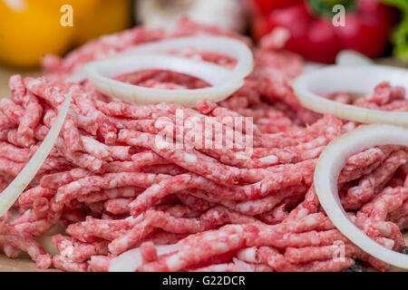 Rohes Hackfleisch / Fleisch und Zwiebel Ringe Nahaufnahme mit frischem Gemüse auf dem Hintergrund Stockfoto