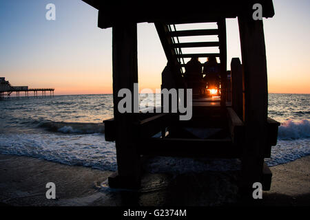 Aberystwyth Wales UK, Montag, 23. Mai 2016 UK Wetter: Leute sitzen auf den Holzsteg am Meer sind Silhouette gegen einen spektakulären Sonnenuntergang über Cardigan Bay in Aberystwyth an der Westküste Wales UK.   Bildnachweis: Keith Morris / Alamy Live News Stockfoto