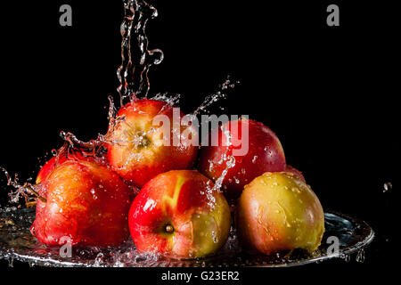 Paar rote Äpfel liegen auf einer silbernen Spitze und fallende Wasser auf einem schwarzen Hintergrund Stockfoto