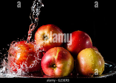 Paar rote Äpfel liegen auf einer silbernen Spitze und fallende Wasser auf einem schwarzen Hintergrund Stockfoto