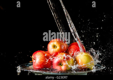 Paar rote Äpfel liegen auf einer silbernen Spitze und fallende Wasser auf einem schwarzen Hintergrund Stockfoto