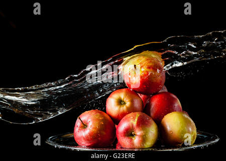 Die wenigen roten Äpfel liegen auf der silbernen Seite und fliegende Wasser auf einem schwarzen Hintergrund Stockfoto