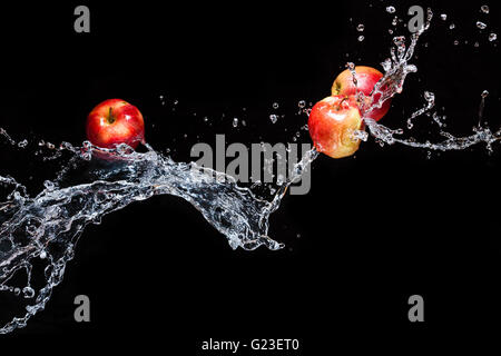 Rote Äpfel, Fliegen im Raum mit dem Wasser auf schwarzem Hintergrund Stockfoto