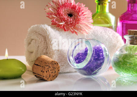 Öle und Badesalz auf weißen Glastisch hautnah. Dekoriert mit Blumen und Handtuch mit braunen Farbverlauf Hintergrund. Stockfoto