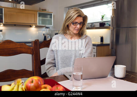 Frau sitzt an einem Tisch ihr Laptop-Bildschirm betrachten. Sie ist zufrieden über Neuigkeiten auf ihrem laptop Stockfoto