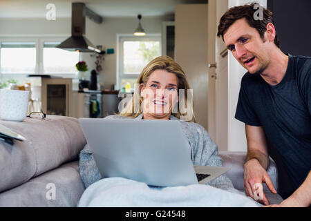 Mann und Frau Ausgabe Zeit zusammen auf der Couch mit einem Laptop, und lächelnd. Mittellange Aufnahme. Stockfoto