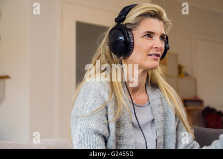 Frau mittleren Alters, die Musik über Kopfhörer hört. Profil. Mittlere Aufnahme. Stockfoto