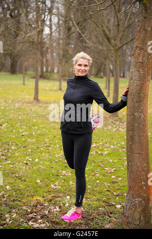 mittleren Alter blonde Frau ihre Beine im Park. Sie ist an einen Baum gelehnt. Stockfoto