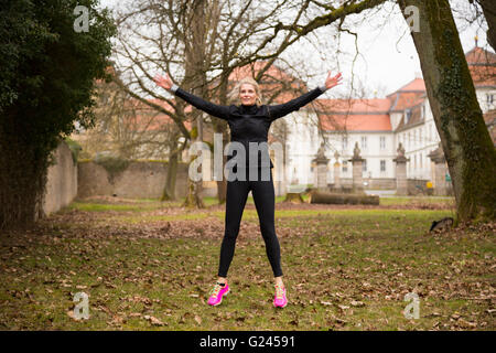 Frau in den 40er Jahren tun Jumping Jacks in einem Herbst Park. Braune Blätter alle um Sie herum. Long Shot. Stockfoto