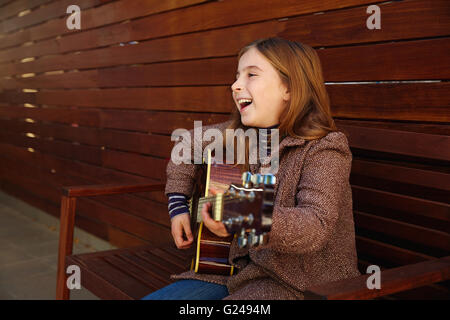 blonde junge Mädchen spielt Gitarre mit Wintermantel auf hölzernen Hintergrund Stockfoto