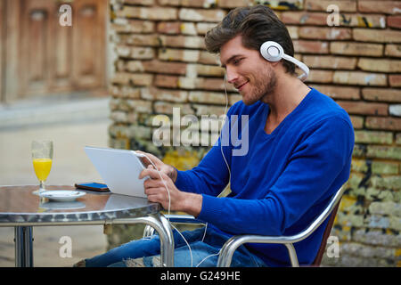 Junger Mann mit TabletPC touch Musik hören im freien sitzend mit Orangensaft Stockfoto