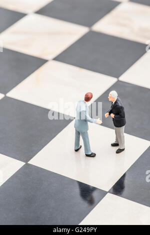 Zwei Figuren von Geschäftsleuten, stehend auf einem Schachbrett Händeschütteln Stockfoto