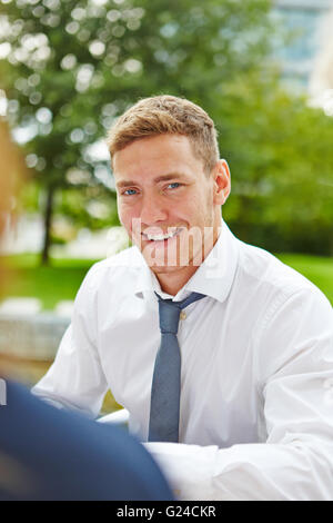 Lächelnde junge Geschäftsmann sitzen im Freien im Sommer Stockfoto