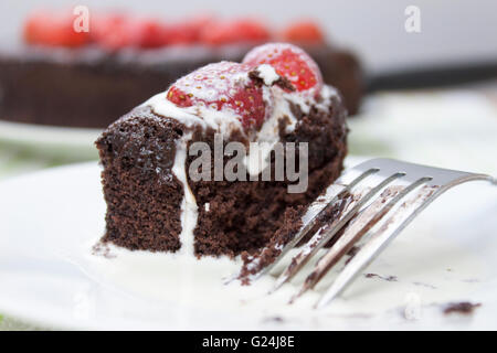 Stück Schokolade Fudge Kuchen garniert mit Reife Erdbeere in frischer Sahne abgedeckt Stockfoto