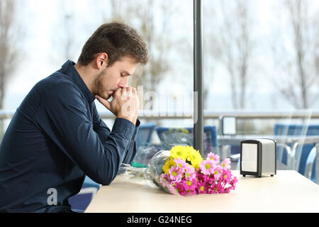 Trauriger Mann mit Blumenstrauß stand ein Datum von seiner Freundin in einem Café Stockfoto