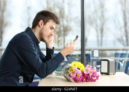 Trauriger Mann mit einem Blumenstrauß stand ein Datum prüfen Telefonnachrichten in einem Coffee-shop Stockfoto