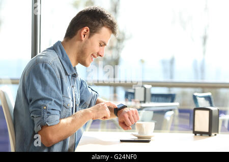 Profil eines Mannes mit einer generischen Smartwatch mit einem Mobiltelefon auf eine Pause in einer Bar mit Getränken Stockfoto