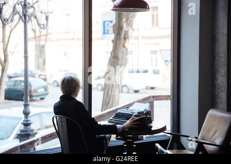 Blonde Mädchen rückwärts in einem Café sitzen und halten einen Hut Stockfoto