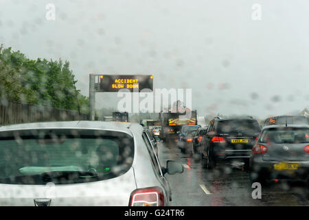 Verkehr-Warteschlange im Regen auf der A20 Annäherung an der Kreuzung mit der M25. Warnschild liest Unfall Slow Down. Stockfoto