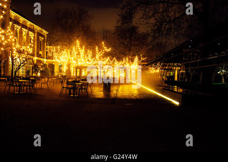 leere Nacht Restaurant, viele Tische und Stühle mit niemand, magische Lichterketten an Bäumen wie Weihnachten Stockfoto